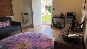 A living room with a large floral rug, a sofa, a coffee table, and a desk with a computer and printer. There is a door leading to a patio area with outdoor furniture. - Charming studio in enchanting Napa walking distance to downtown (Napa)