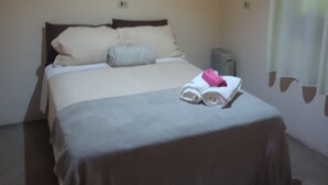 A bedroom with a bed, pillows, a bedside table, and a window with curtains. - Little house in the mountains (Gonçalves)