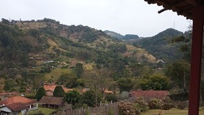 A view from a covered balcony overlooking a rural landscape with houses and hills. - Little house in the mountains (Gonçalves)