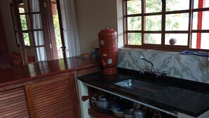 A kitchen with a black countertop, a red water heater, a sink, and a window with a view of greenery. - Little house in the mountains (Gonçalves)