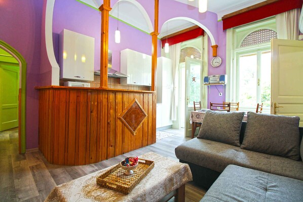 Une pièce comprenant un bar en bois, un canapé, une table à manger et un téléviseur.