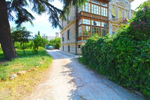 Un étroit sentier pavé mène à un bâtiment historique doté de grandes fenêtres et d’un balcon.