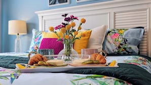 A neatly arranged breakfast tray on a bed with a floral bedspread, a vase of flowers, and a bedside lamp.