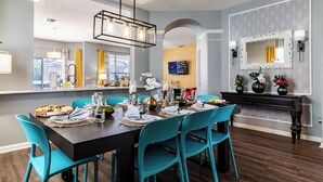 A dining area with a dark wooden table set for six, turquoise chairs, and a modern chandelier.