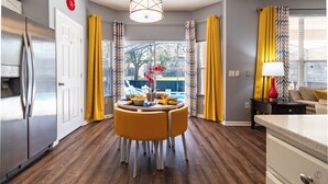 A modern kitchen with a dining area, wooden flooring, and a view of a backyard.