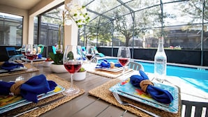 A dining table set with placemats, napkins, and wine glasses, overlooking a swimming pool.