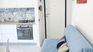A compact living space with a kitchenette, a blue sofa, and a chair. - CN001 - Cesenatico, two-room apartment with balcony and air conditioning (Cesenatico)