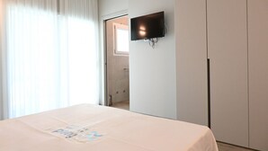 Habitació d'hotel amb llit, televisió penjada a la paret, porta que dona a un bany i finestra amb cortines.