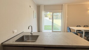 Cuina amb rentatge, taula de dinar, cadires i vista a un jardí verd i un edifici a través d'una porta de vidre.