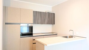 Una cuina moderna amb forn integrat, un rentataps i armaris de tons clars.