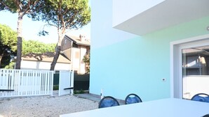 Taula blanca amb caires blaus, una tanca blanca i arbres al fons.