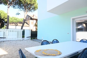 A white table with blue chairs, a white fence, and trees in the background.
