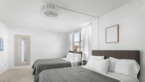 A hotel room with two beds, a large window, a ceiling fan, and a framed picture on the wall. - Bay Harbor Sunset Apt 4A (Bay Harbor Islands)