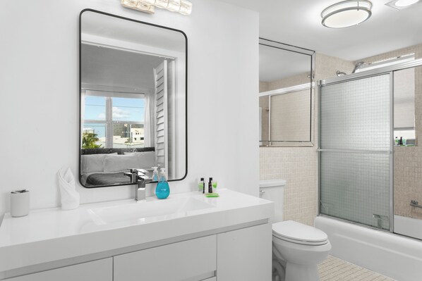 Une salle de bain moderne avec un lavabo blanc, un grand miroir, des toilettes et une douche à parois de verre.