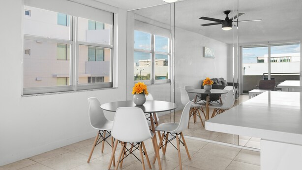 A modern kitchen with white cabinetry, a central island, and a dining area with white chairs and a round table. - Bay Harbor Sunset Apt 4A (Bay Harbor Islands)