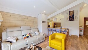 Una sala moderna con sofá, un sillón amarillo y un comedor con taburetes de bar.