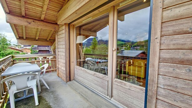 Un balcón de madera con una mesa y sillas, con vistas a un paisaje montañoso.
