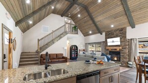 A spacious living area with a kitchen island, a fireplace, and a staircase leading to an upper level.