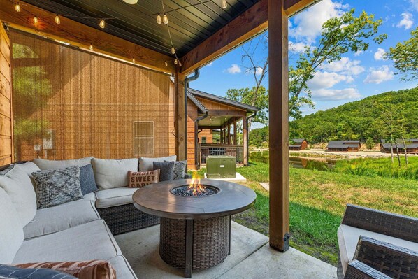 An outdoor seating area with a fire pit, a covered patio, and a view of a cabin and forest.