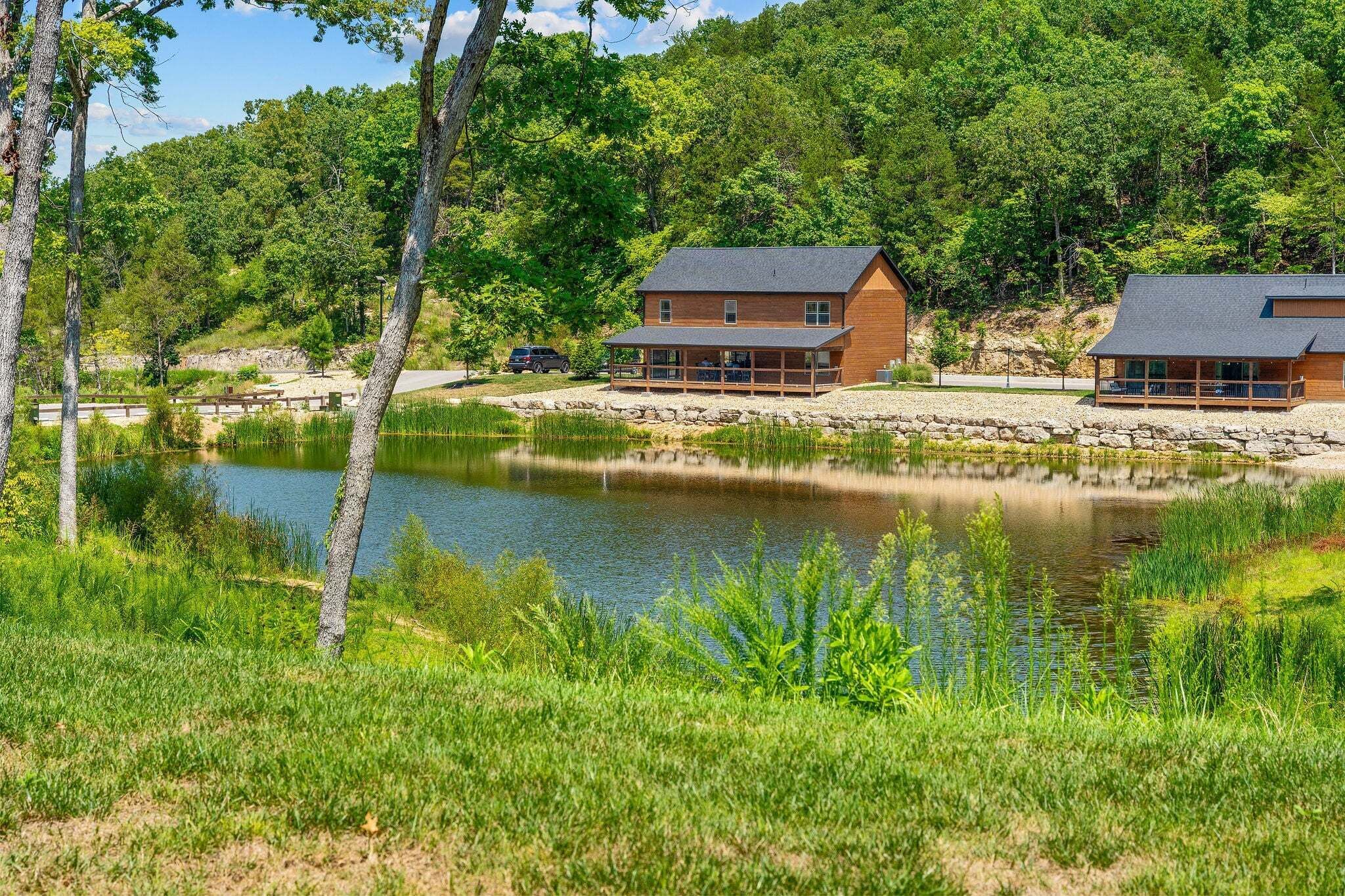 A cabin with a deck overlooking a lake, surrounded by lush greenery and trees.