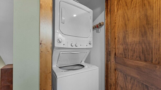A compact laundry room with a washing machine and dryer, wooden door frame, and a small shelf with a bottle. - Private Hot Tub Cabin Near Table Rock Lake with Firepit, Free Tickets & Community Experiences (Hollister)