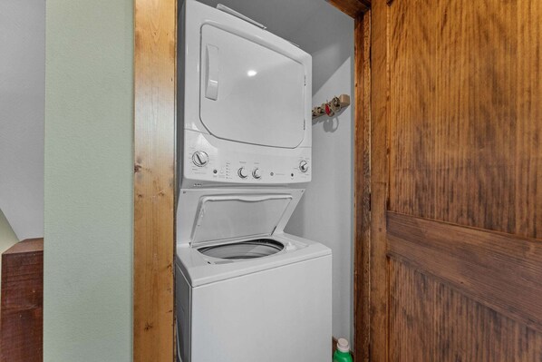 A compact laundry room with a washing machine and dryer, wooden door frame, and a small shelf with a bottle.