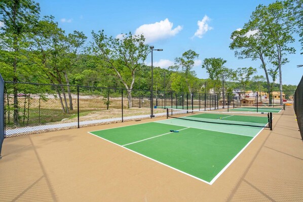 A tennis court with a net, surrounded by a fence and trees.