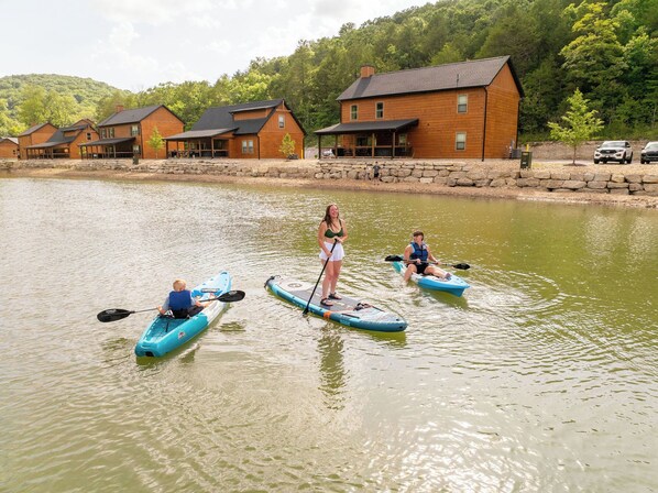 A lakeside setting with paddleboards, a wooden cabin, and a stone wall.