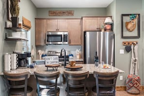 Una cocina con armarios de madera, electrodomésticos de acero inoxidable, una zona de bar con taburetes y un cartel que dice 'DON'T CARE I'M CAMPING'.