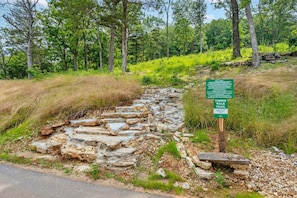 Ein Kiesweg führt durch ein bewaldetes Gebiet, mit einem Schild, das einen Holzsteg-Wanderweg kennzeichnet.