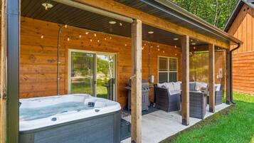 En træhytte med jacuzzi, udendørs møbler og en overdækket terrasse.