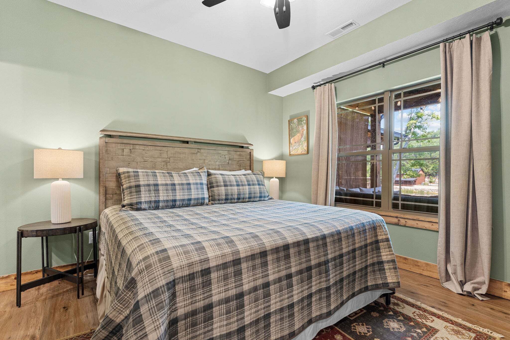 A bedroom with a bed, two bedside tables, a window with curtains, and a ceiling fan.
