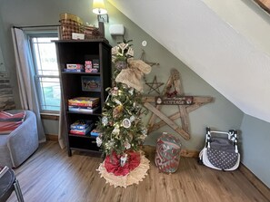 A cozy room with a Christmas tree, a bookshelf with games, a star decoration, and a stroller.