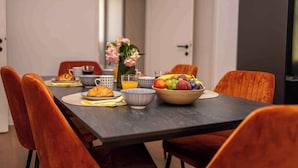 Ein Esstisch mit orangefarbenen Stühlen, eine Obstschale, ein Croissant und ein Glas Orangensaft.
