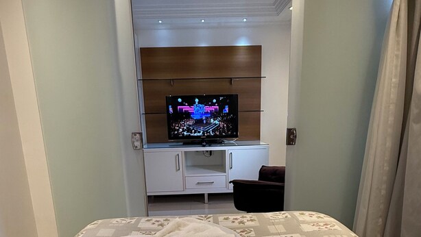 Habitación de hotel con cama, televisor en un mueble y baño visible a través de una puerta abierta.
