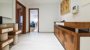 Un hall d’hôtel moderne avec un comptoir d’accueil en bois, une cloison en verre et une vue sur un espace de détente agrémenté d’un canapé bleu.