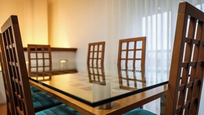 Un coin repas avec une table à plateau en verre, des chaises en bois et un coussin de couleur turquoise.