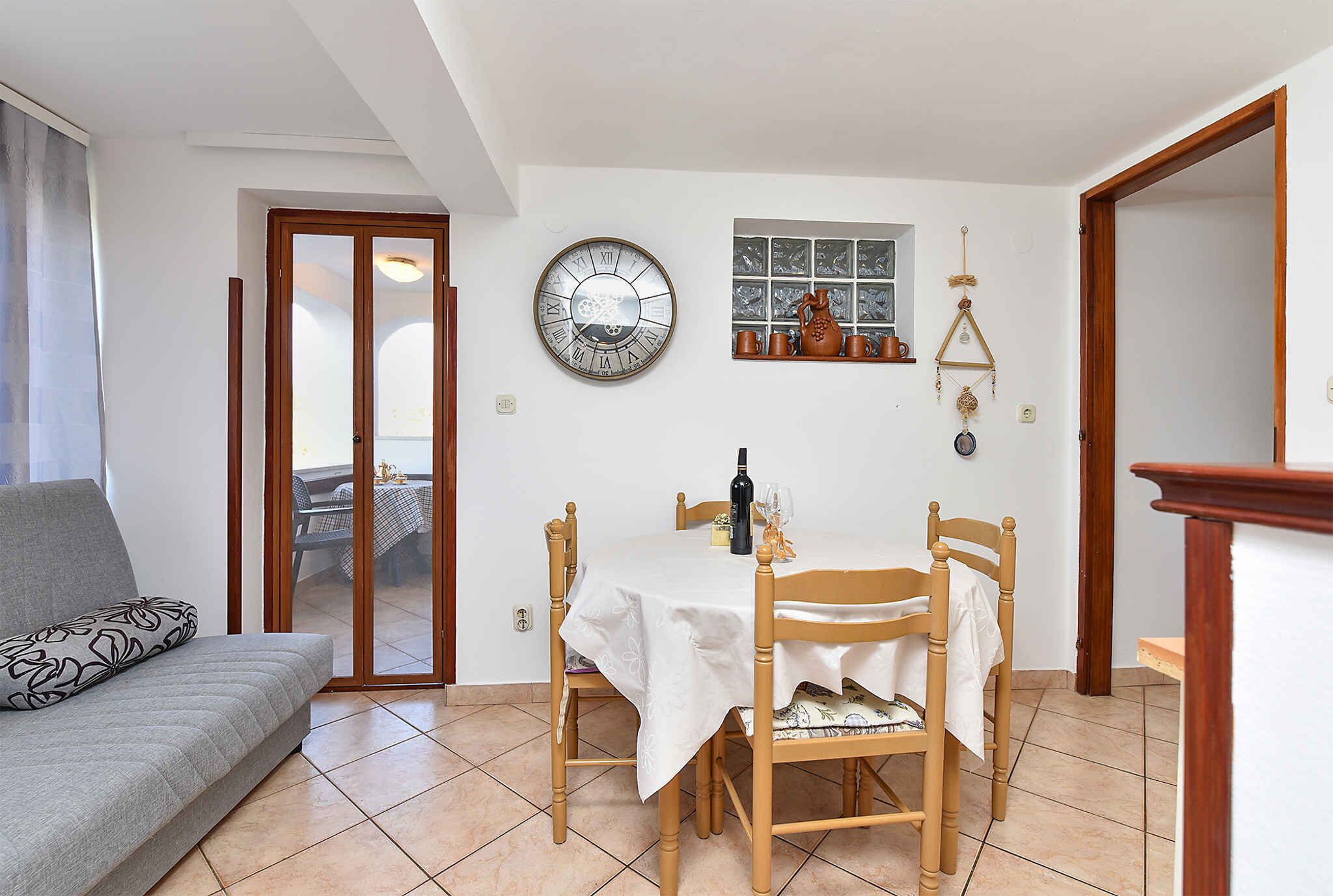 A dining area with a table set for two, a wooden chair, and a sofa with a patterned cushion.