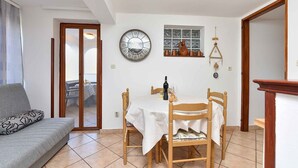 Un coin repas avec une table dressée pour deux personnes, une chaise en bois et un canapé agrémenté d’un coussin à motifs.