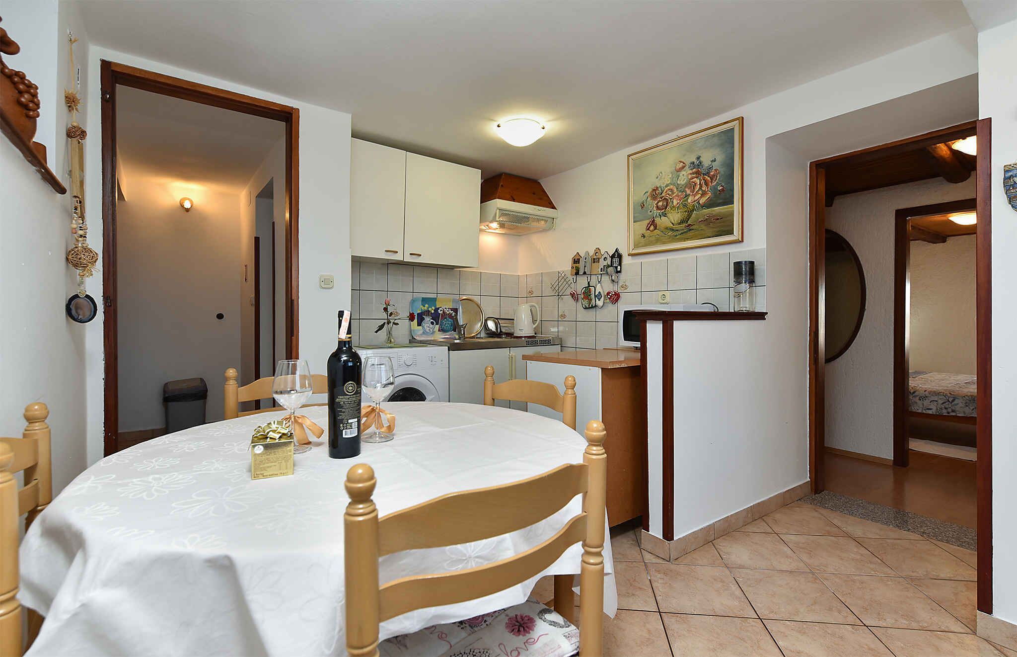 Un comedor con una mesa preparada para dos, una cocina al fondo y un cuadro en la pared.