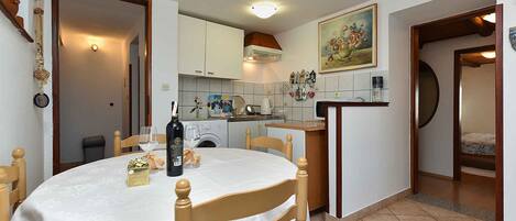 Un comedor con una mesa preparada para dos, una cocina al fondo y un cuadro en la pared.
