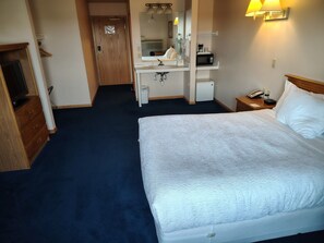 Ein Hotelzimmer mit einem großen Bett, einem Schreibtisch mit Spiegel, einer Mikrowelle und einem Telefon auf dem Nachttisch.