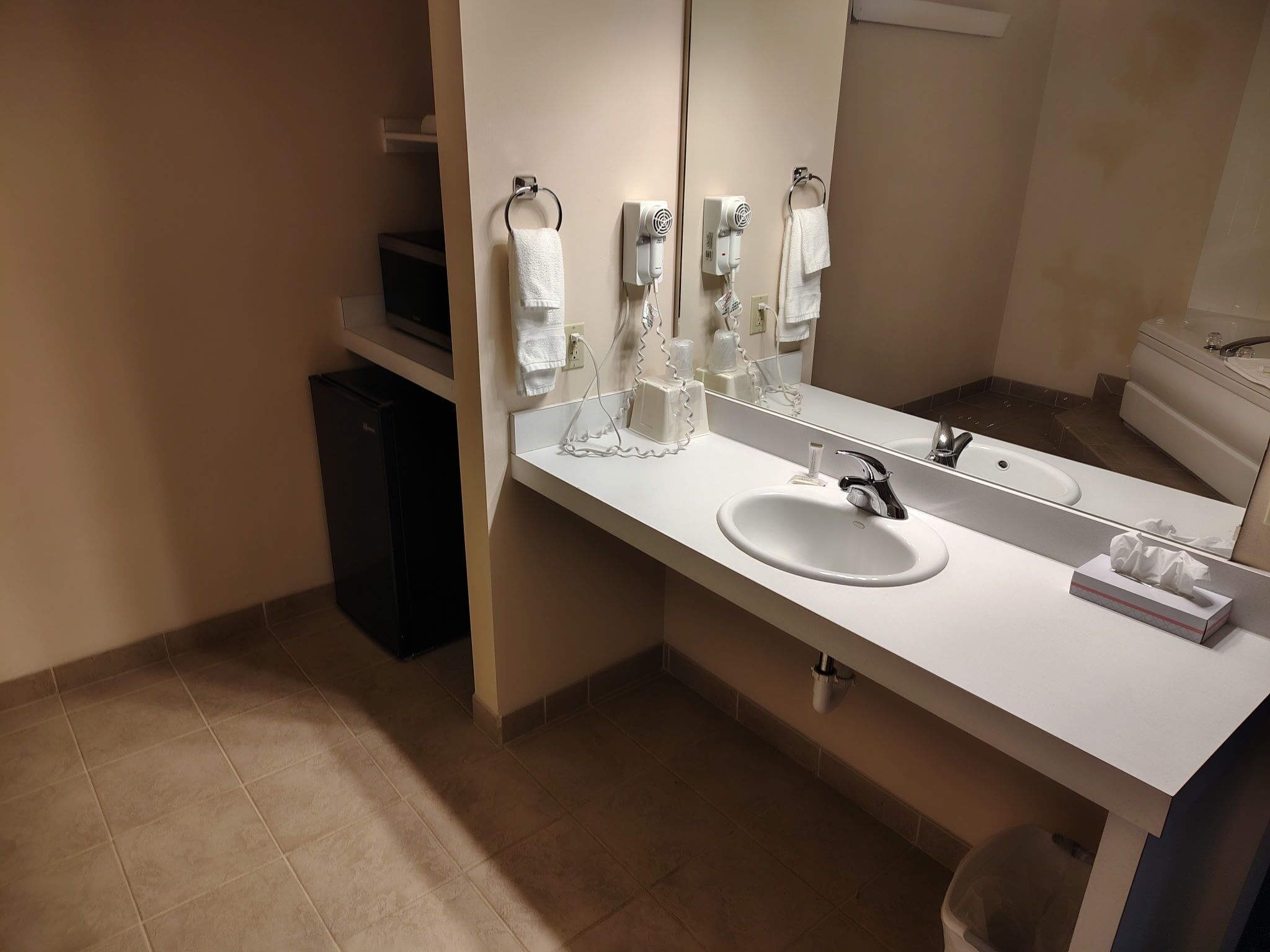 Un baño moderno con un lavamanos blanco, un espejo grande y dos secadores de pelo montados en la pared.