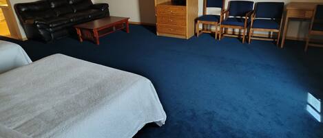 Una habitación con una cama grande, un sofá de cuero negro, un armario de madera y varias sillas azules.
