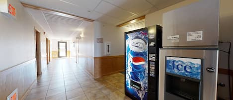 Un pasillo de hotel con un letrero de salida, una máquina expendedora y un dispensador de hielo.