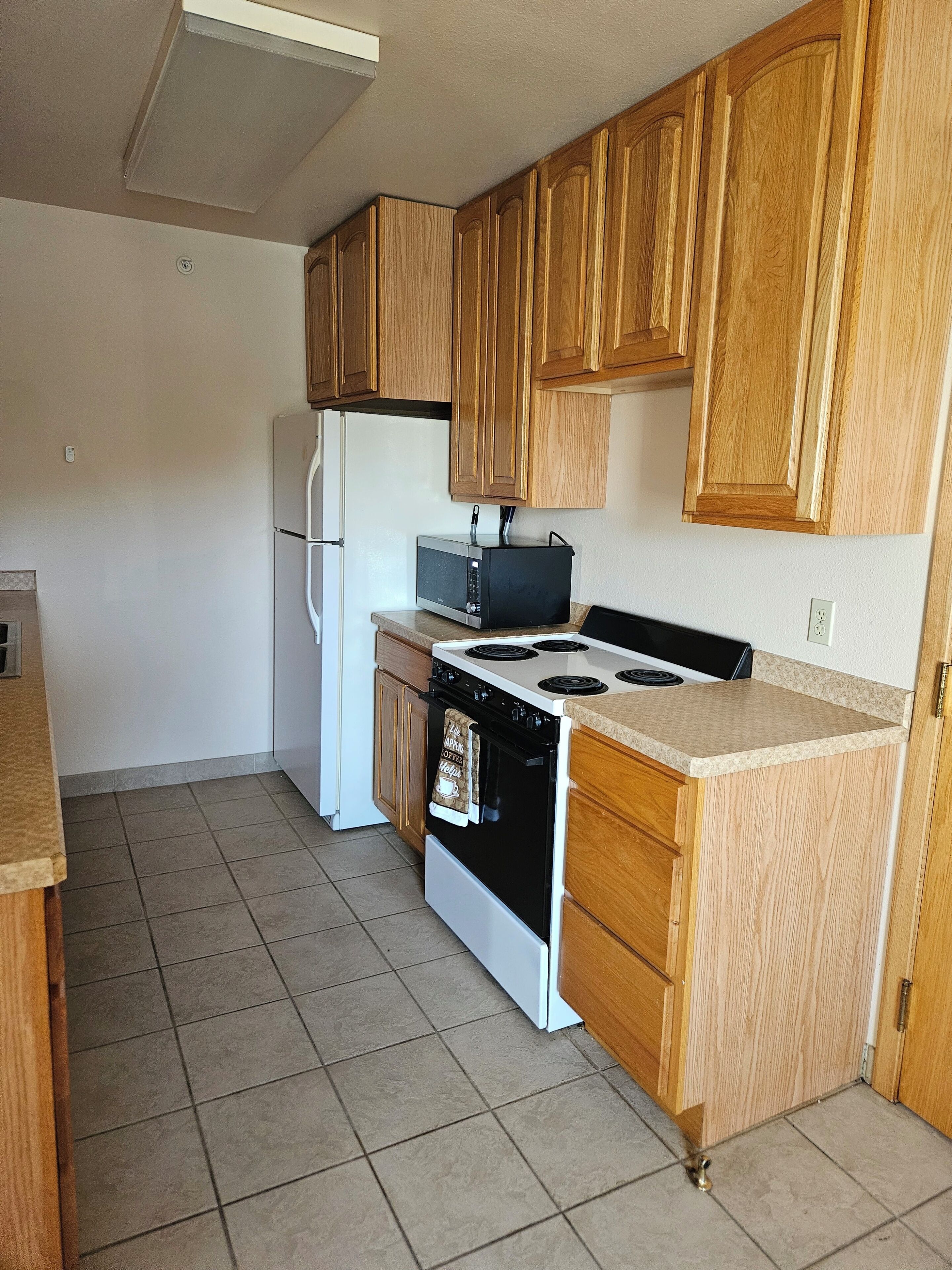 A kitchen with wooden cabinets, a white refrigerator, a microwave, a stove, and a tiled floor.