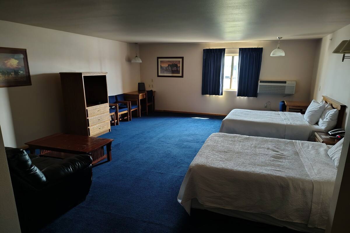 Ein Hotelzimmer mit zwei Betten, einem Schreibtisch, einem Stuhl, einem Fernseher und einem großen Fenster mit Vorhängen.