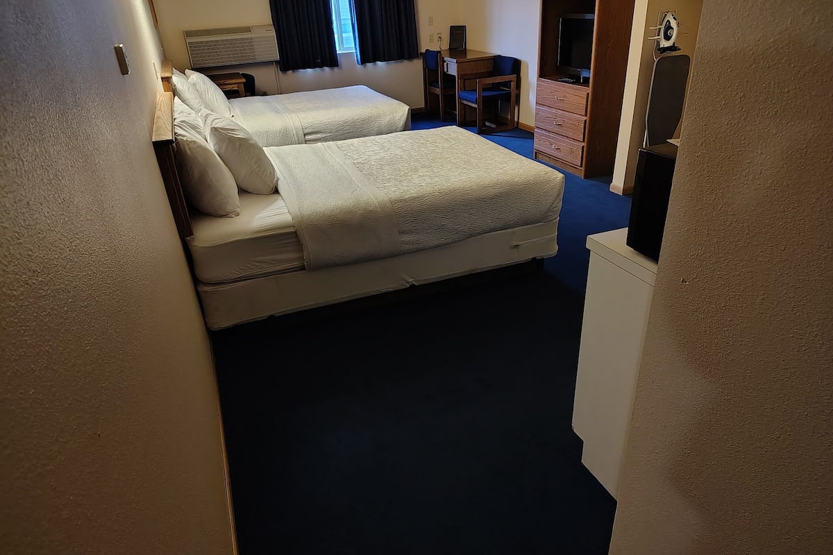 Habitación de hotel con dos camas, un escritorio, un aparador y una televisión.
