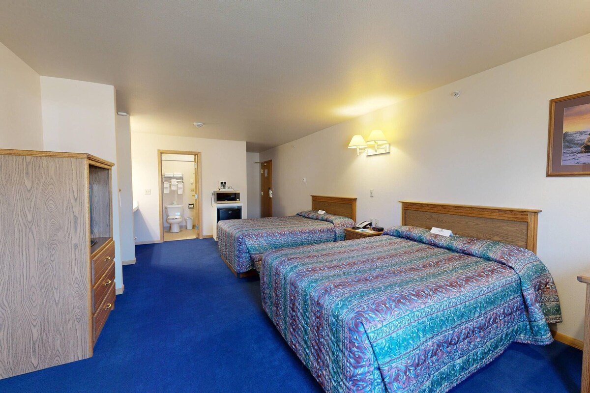 Habitación de hotel con dos camas, un escritorio, una silla, un armario y un baño.