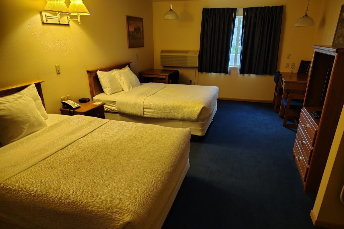 Habitación de hotel con dos camas, un escritorio, un aparador y una ventana con cortinas.